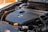 Close-up view of a car engine showing the engine cover with a manufacturer's logo and the text indicating specifications. The surrounding components of the engine are visible, such as wires, hoses, and caps.