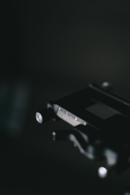 A close-up view of a caliper with a focus on the metal scale and dial, set against a dark blurred background. The lighting highlights the precision tool's measurements and metallic finish.