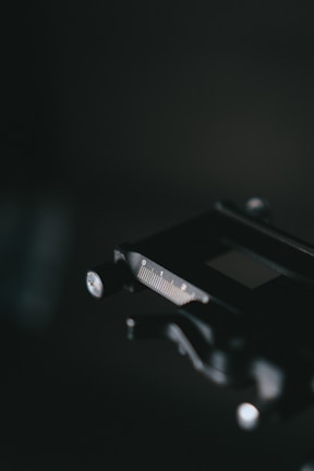 A close-up view of a caliper with a focus on the metal scale and dial, set against a dark blurred background. The lighting highlights the precision tool's measurements and metallic finish.