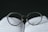 A pair of round-framed eyeglasses is placed on top of an open book. The glasses are positioned in a way that the lenses appear to magnify the text beneath them. The background is dark, creating a strong contrast with the white pages and the clear lenses of the glasses.