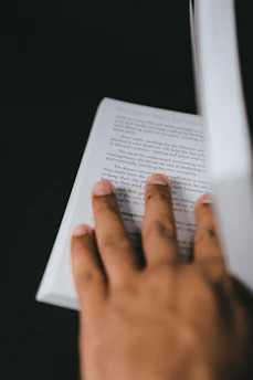 Close-up of a braille transcriptionist's hands gently reading a fresh braille page under soft lighting.