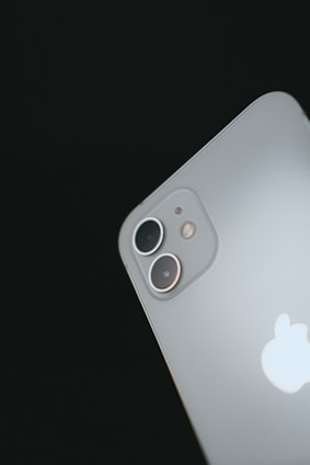 A close-up view of a sleek smartphone focusing on its dual camera lenses at the back. The Apple logo is prominently displayed below the cameras, and the surface is smooth and metallic.