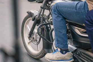 Close-up of a biker's foot wearing a sneaker protector while changing gears on a motorcycle.