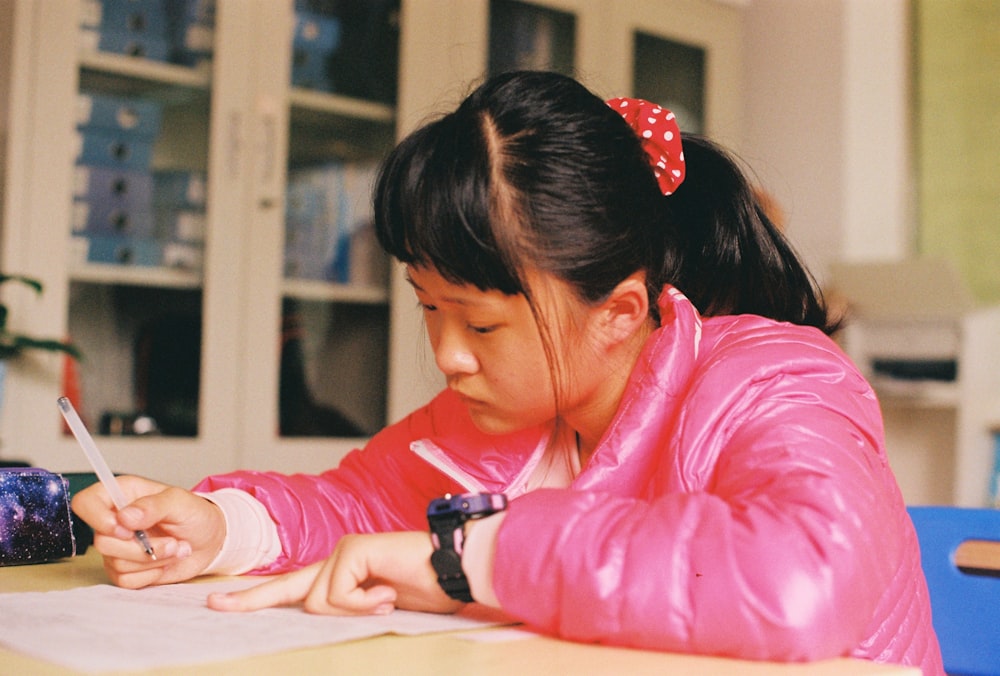 girl in pink jacket sitting at table