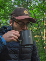 A traveler holding a Frostara tumbler while hiking in a misty forest.