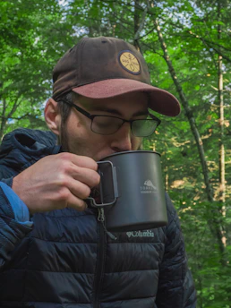 A traveler holding a Frostara tumbler while hiking in a misty forest.