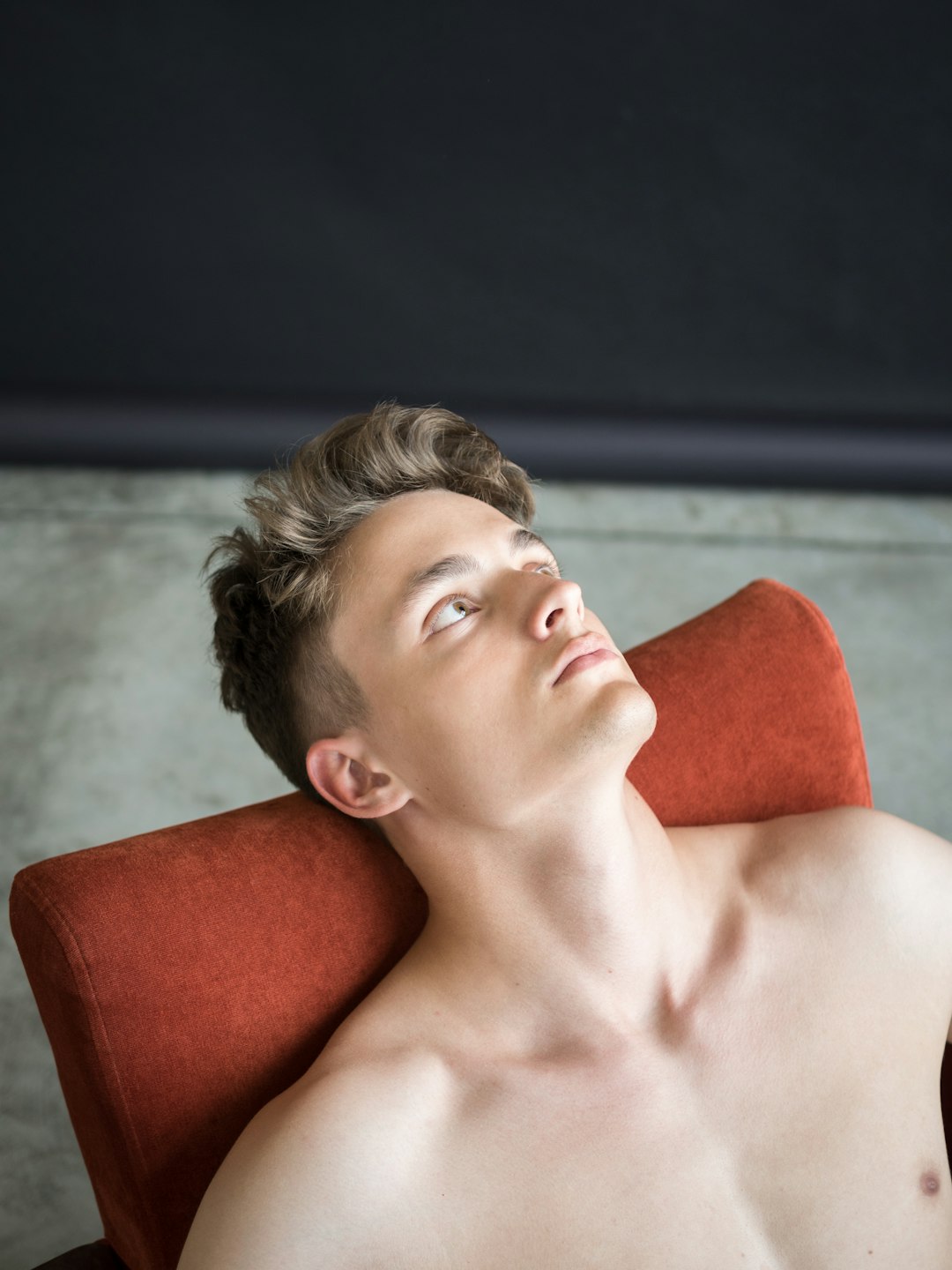 topless man lying on red sofa