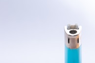 A close-up of a lighter featuring a metallic ignition wheel and a turquoise body against a light gray background.