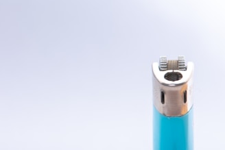 A close-up of a lighter featuring a metallic ignition wheel and a turquoise body against a light gray background.