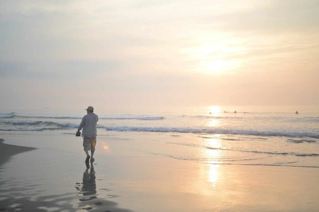 man in white shirt and black pants walking on beach during sunset