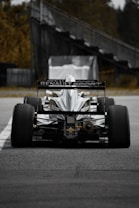 A high-performance race car with the Renault Sport logo displayed prominently on the back. The car is stationary on a track, viewed from behind, with large, smooth treaded tires. In the background, there is a blurred structure and some greenery.