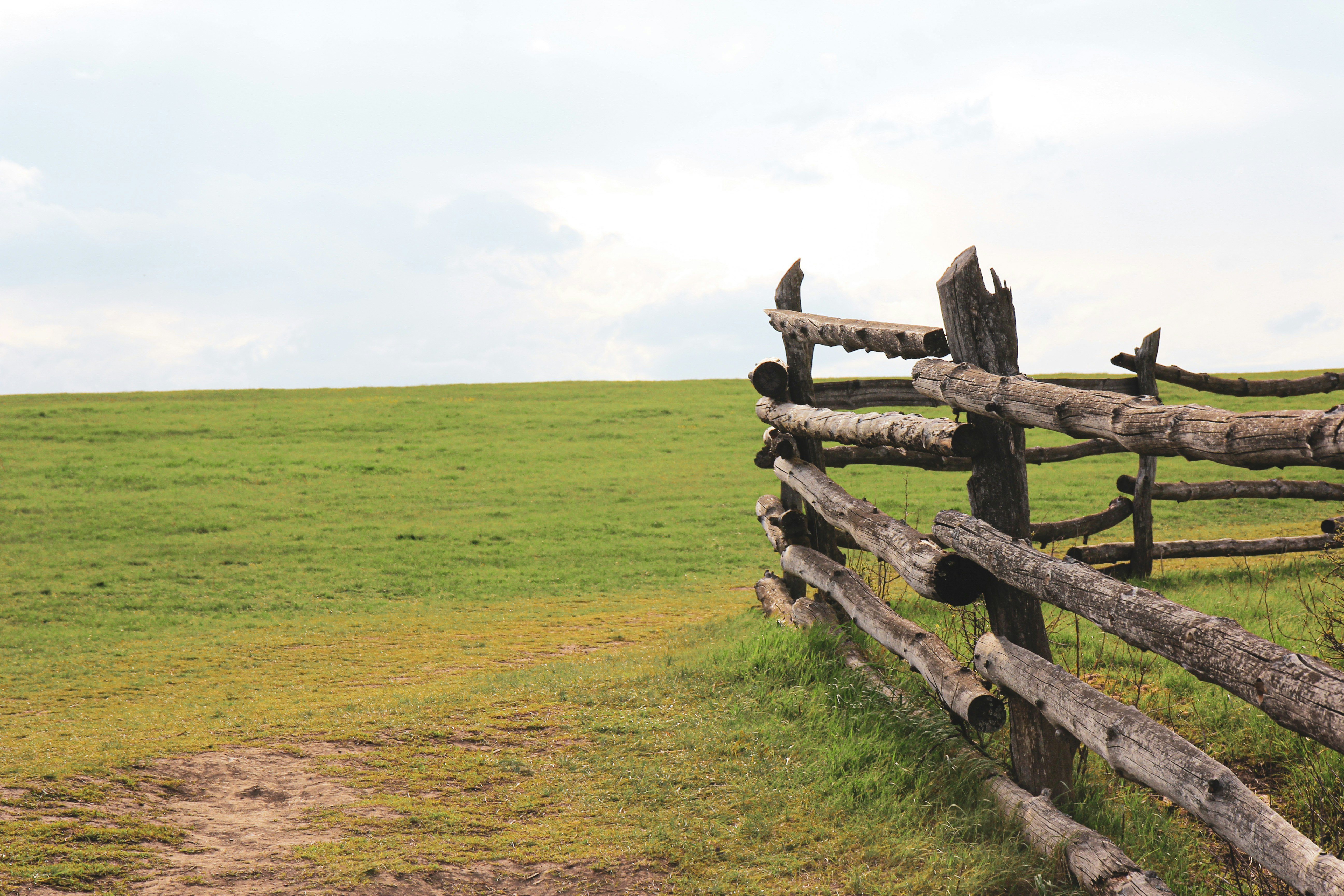 brown wooden fence on green grass field under white cloudy sky during daytime