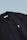 This is a close-up image of a black polo shirt with a collar and two buttons. There is a small embroidered design on the chest, consisting of two overlapping shapes in light blue. The label inside the collar reads 'SCAMBIO'. The background is a simple gradient from pale blue to white.