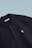 This is a close-up image of a black polo shirt with a collar and two buttons. There is a small embroidered design on the chest, consisting of two overlapping shapes in light blue. The label inside the collar reads 'SCAMBIO'. The background is a simple gradient from pale blue to white.