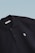 This is a close-up image of a black polo shirt with a collar and two buttons. There is a small embroidered design on the chest, consisting of two overlapping shapes in light blue. The label inside the collar reads 'SCAMBIO'. The background is a simple gradient from pale blue to white.