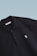 This is a close-up image of a black polo shirt with a collar and two buttons. There is a small embroidered design on the chest, consisting of two overlapping shapes in light blue. The label inside the collar reads 'SCAMBIO'. The background is a simple gradient from pale blue to white.