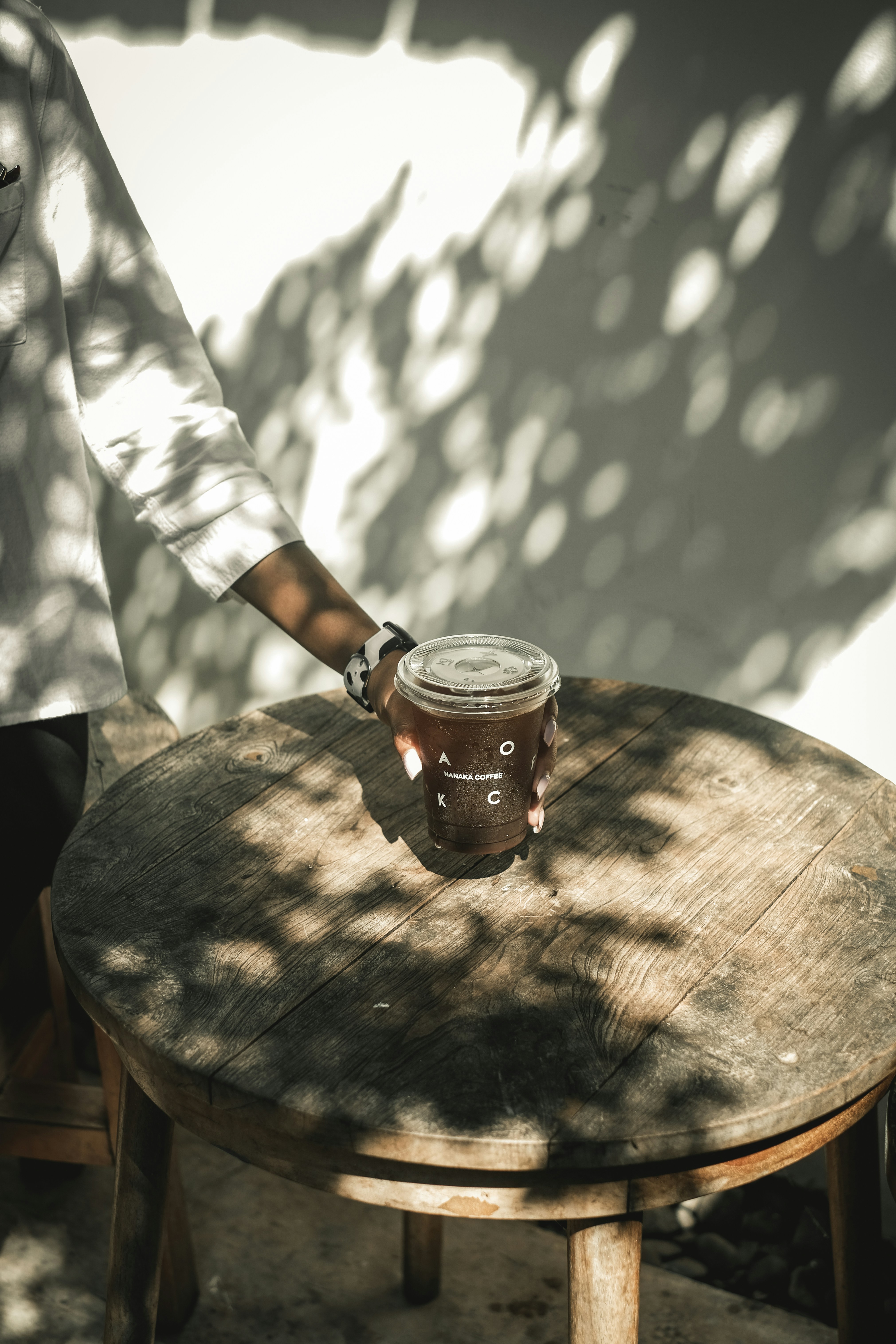 person in white and black checked shirt holding clear glass mug with brown liquid on brown
