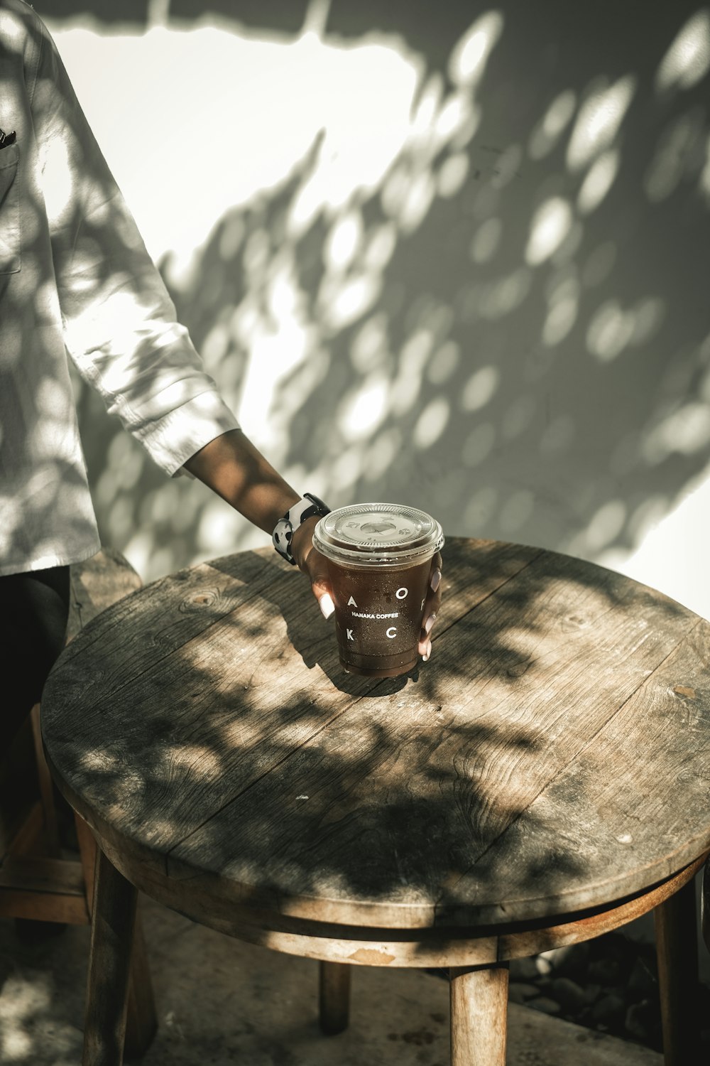 person in white and black checked shirt holding clear glass mug with brown liquid on brown