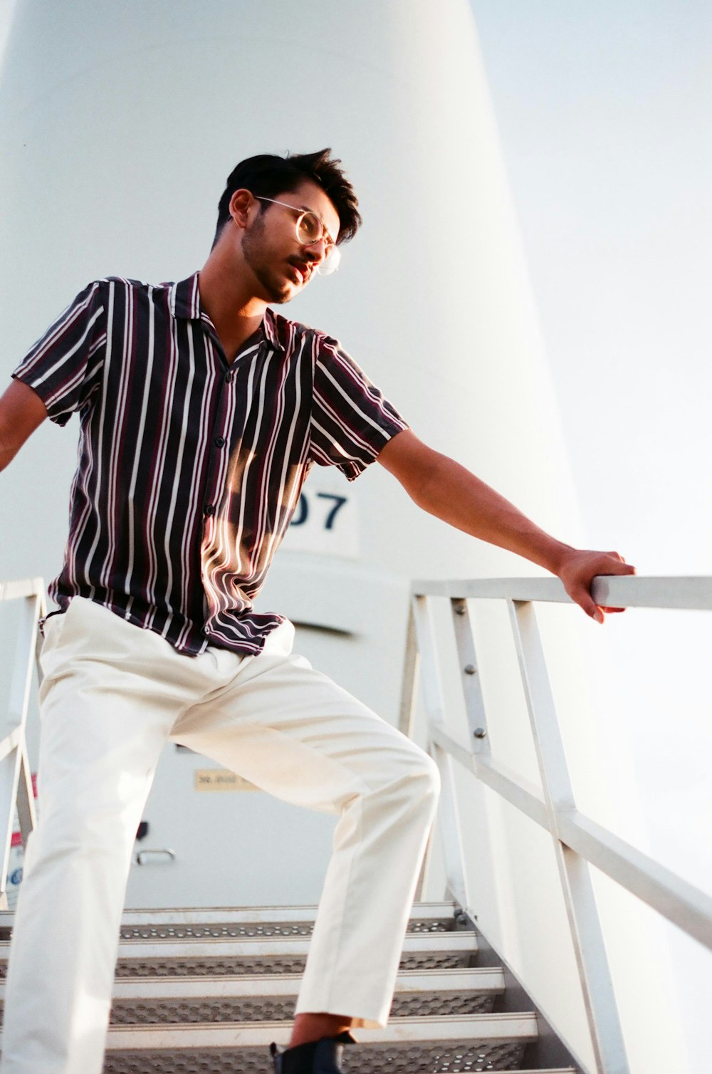 man in black and white stripe shirt and white pants sitting on white wooden staircase