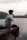 man in grey t-shirt and black pants sitting on brown rock near body of water