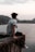 man in grey t-shirt and black pants sitting on brown rock near body of water