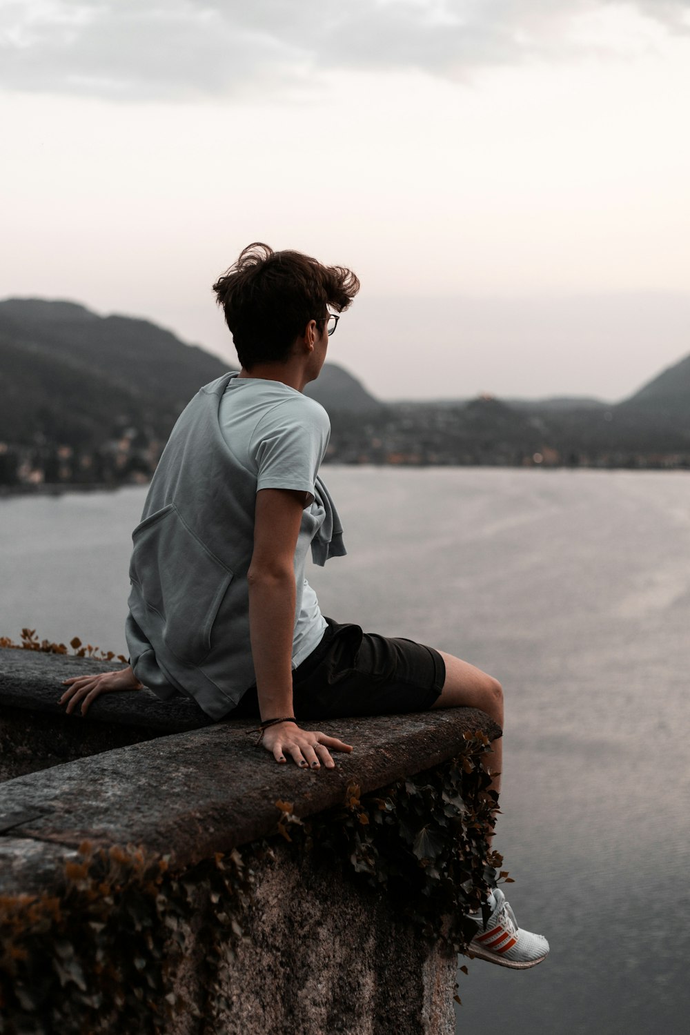 man in grey t-shirt and black pants sitting on brown rock near body of water