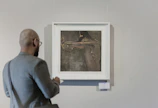 Close-up of a visitor thoughtfully observing a bold, expressive queer portrait hanging on a pristine white wall.