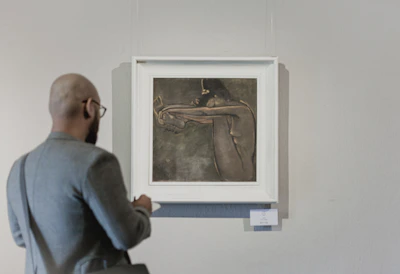 Close-up of a visitor thoughtfully observing a bold, expressive queer portrait hanging on a pristine white wall.