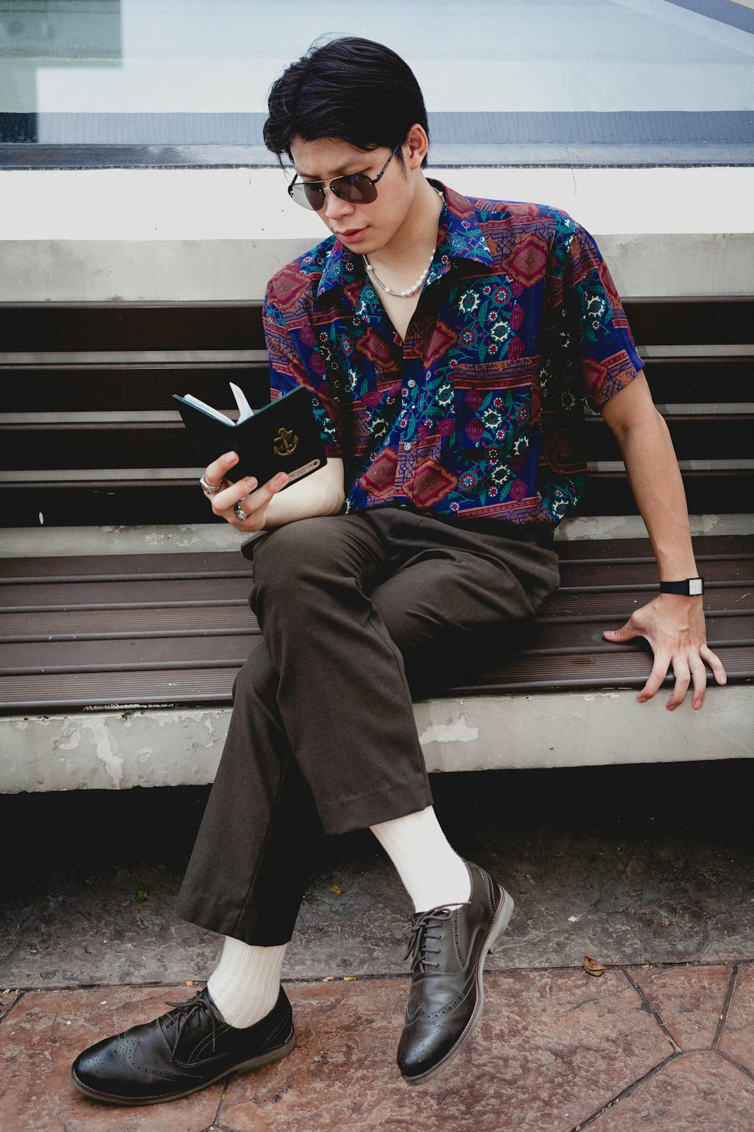 man in red blue and white button up shirt and black pants sitting on brown wooden