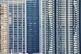 Tall high-rise buildings with numerous glass windows and balconies are tightly packed together, emphasizing urban density. The architecture features modern design elements with vertical lines and repetitive patterns.