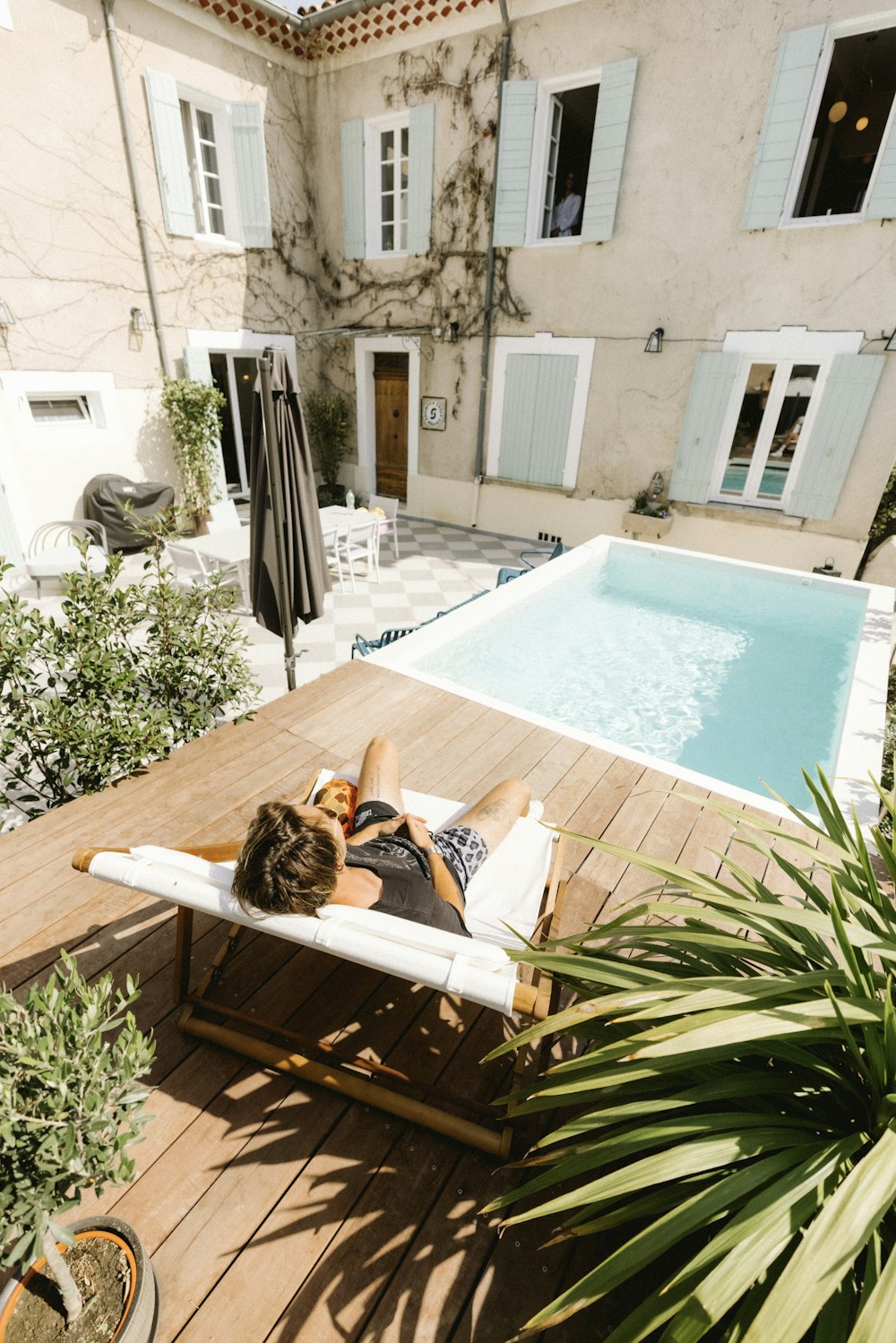 woman in white shirt lying on white lounge chair beside swimming pool during daytime