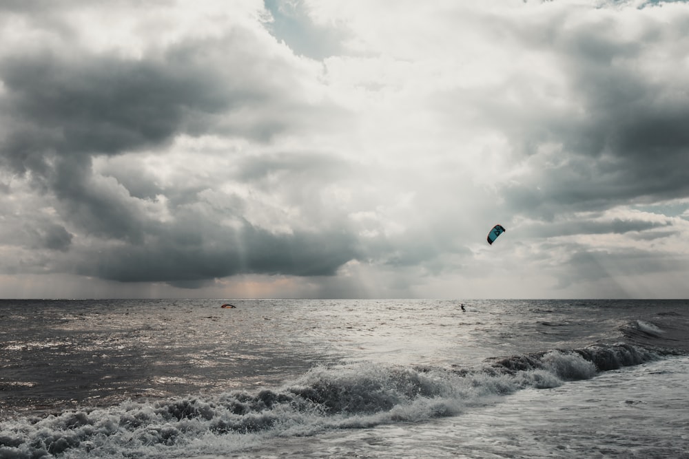person surfing on sea waves under white clouds during daytime