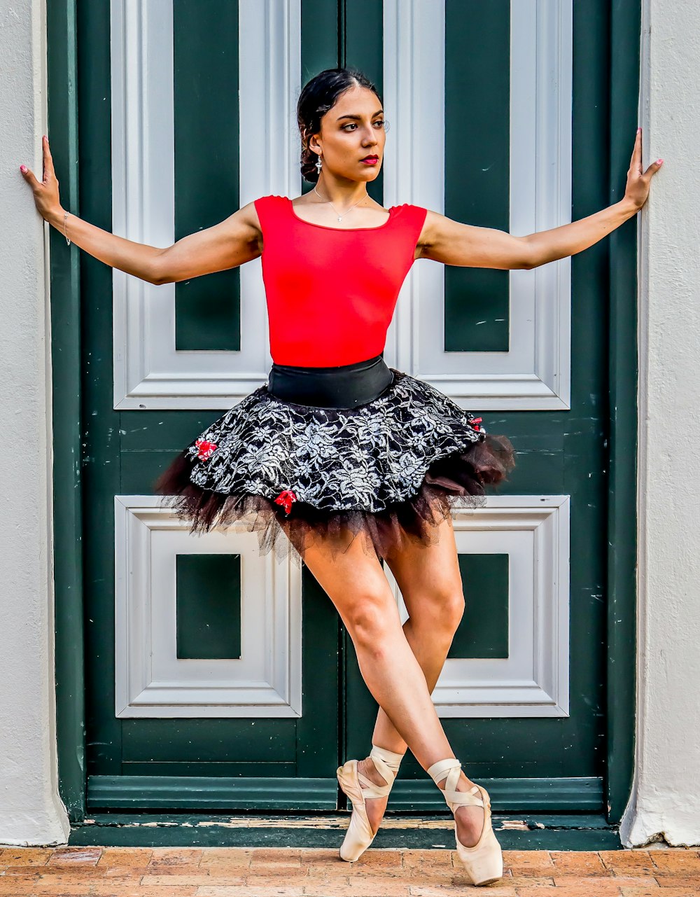 woman in red tank top and black skirt standing beside gray wooden door