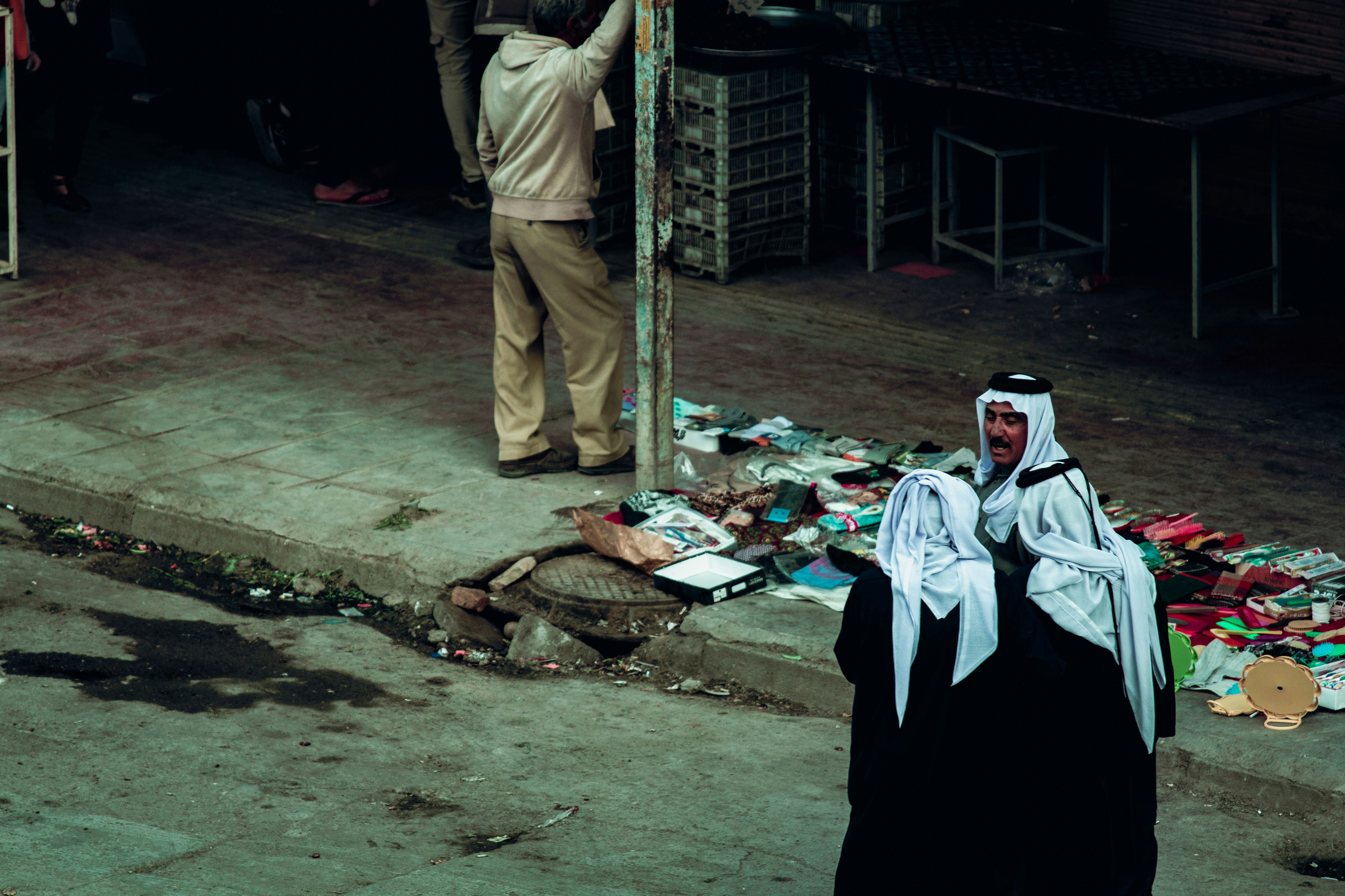 man in brown jacket and white cap standing near man in black thobe