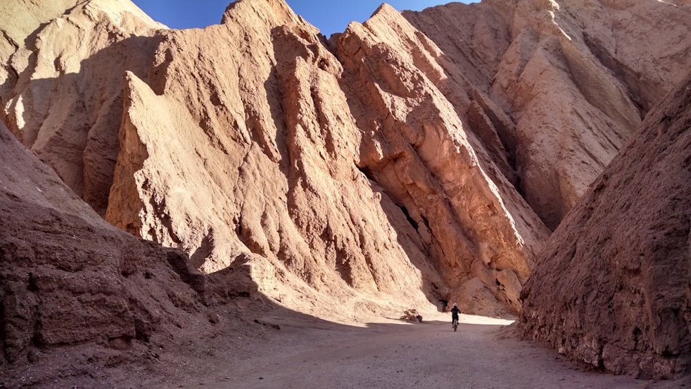 person walking on beach near brown rock formation during daytime