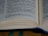 An open book displaying text on both visible pages, with a focus on specific paragraphs. The pages are slightly curved, resting on a wooden surface, and there is a blue bookmark ribbon partially visible between the pages.