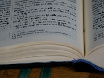 An open book displaying text on both visible pages, with a focus on specific paragraphs. The pages are slightly curved, resting on a wooden surface, and there is a blue bookmark ribbon partially visible between the pages.