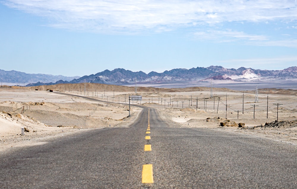 gray concrete road near brown mountain under blue sky during daytime