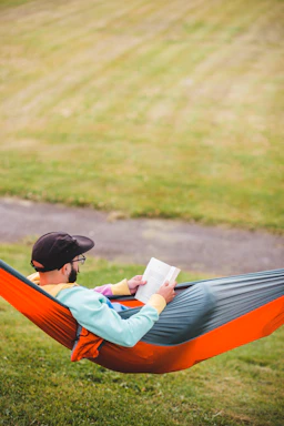 Outdoor hammock between two trees with someone reading a book.
