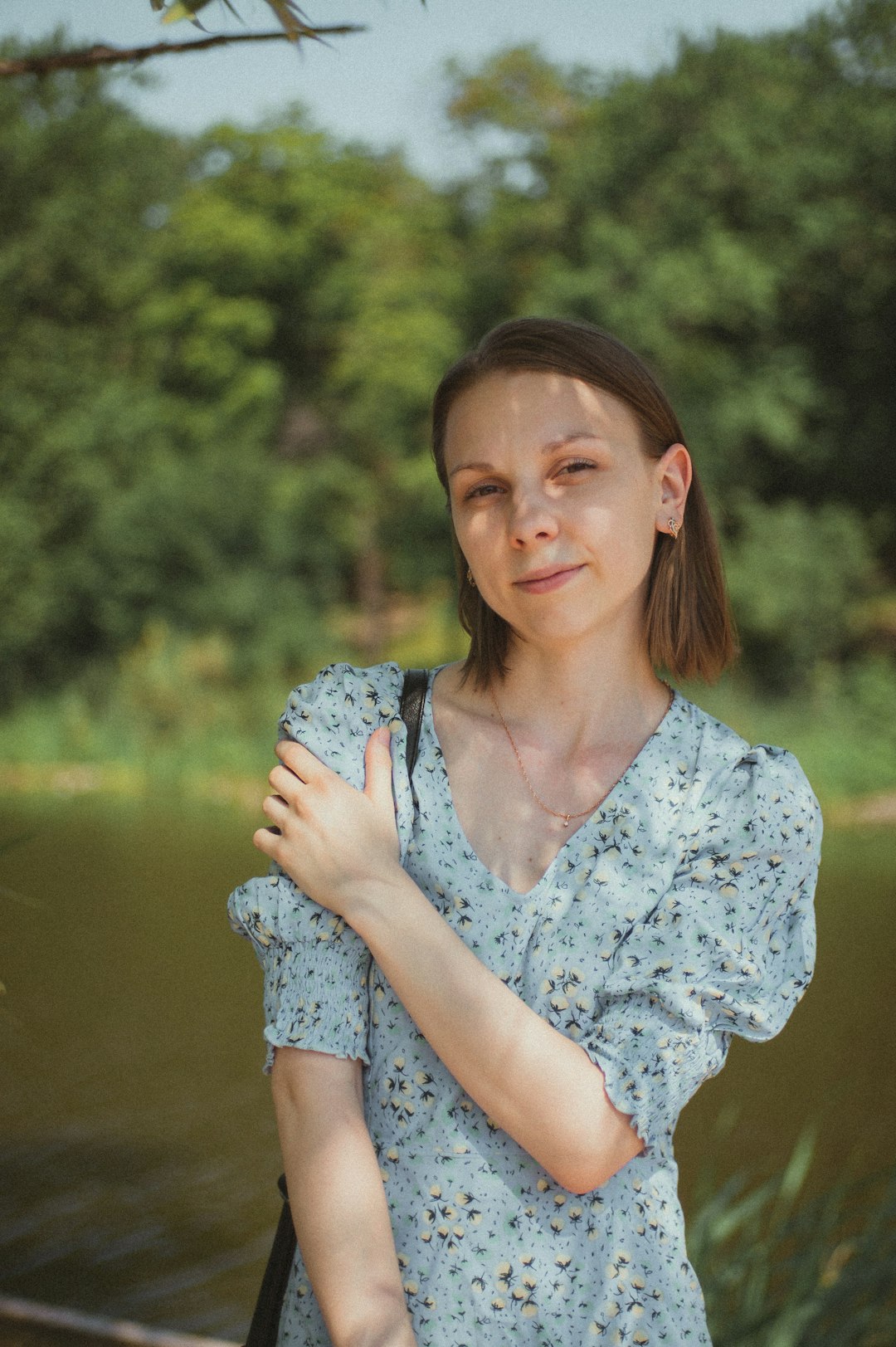 woman in white and blue floral shirt standing near lake during daytime
