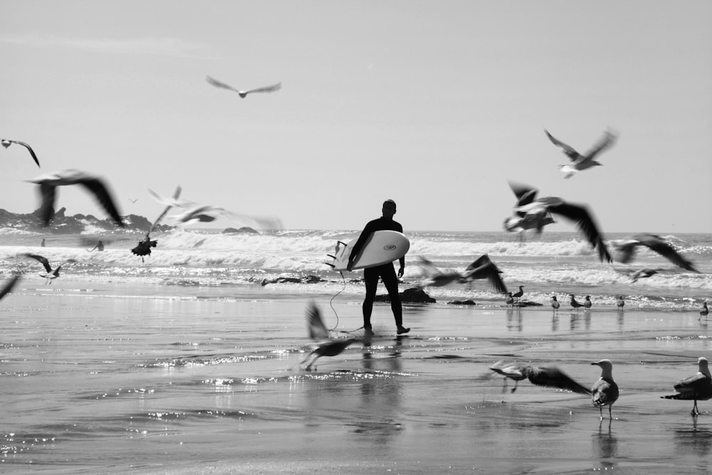 Graustufenfoto einer Frau in schwarzem Tanktop, die mit Vögeln am Strand spazieren geht