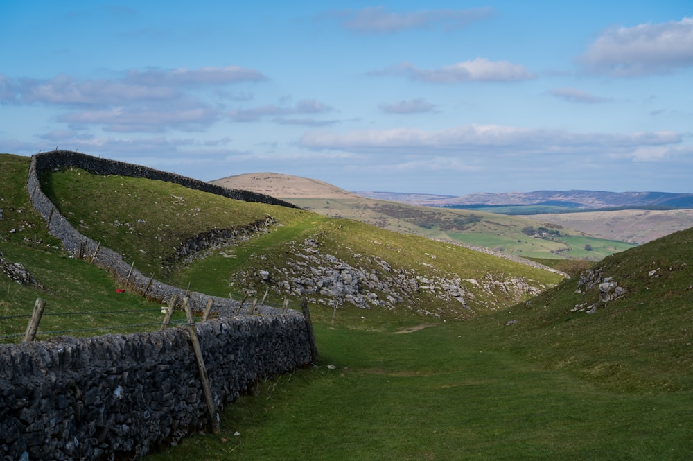 green grass field and mountain under white clouds and blue sky during daytime