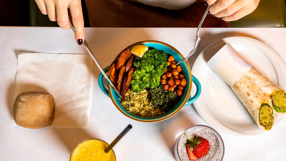 Person, die einen silbernen Löffel und eine blaue Keramikschüssel mit Essen hält