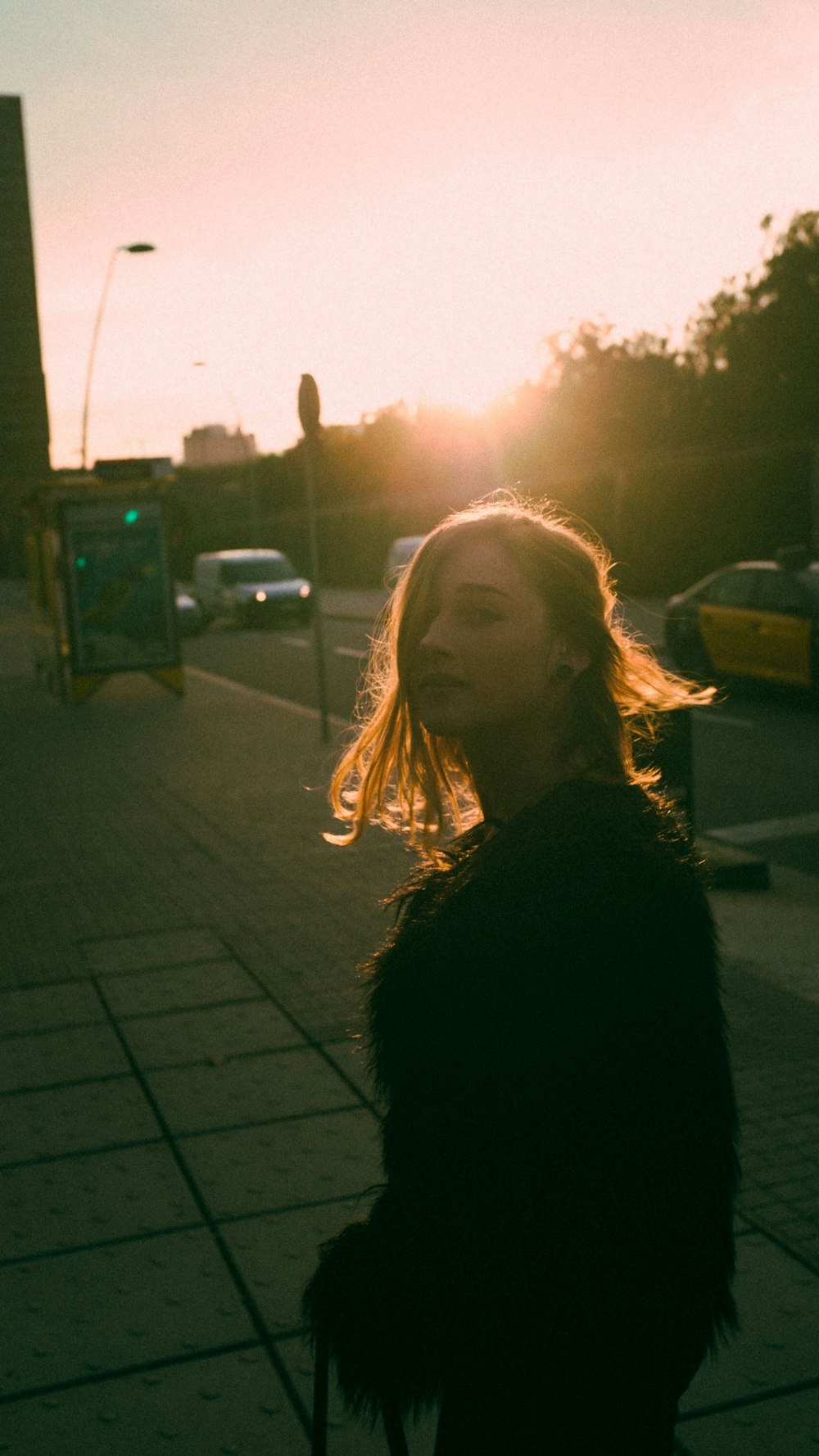 woman in black jacket standing on sidewalk during daytime