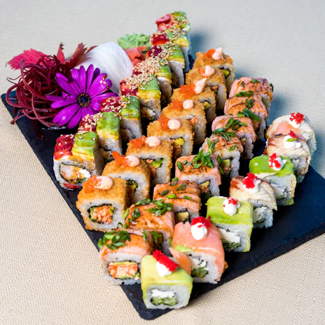 Artfully arranged nigiri and maki rolls on a black slate board with delicate garnishes.