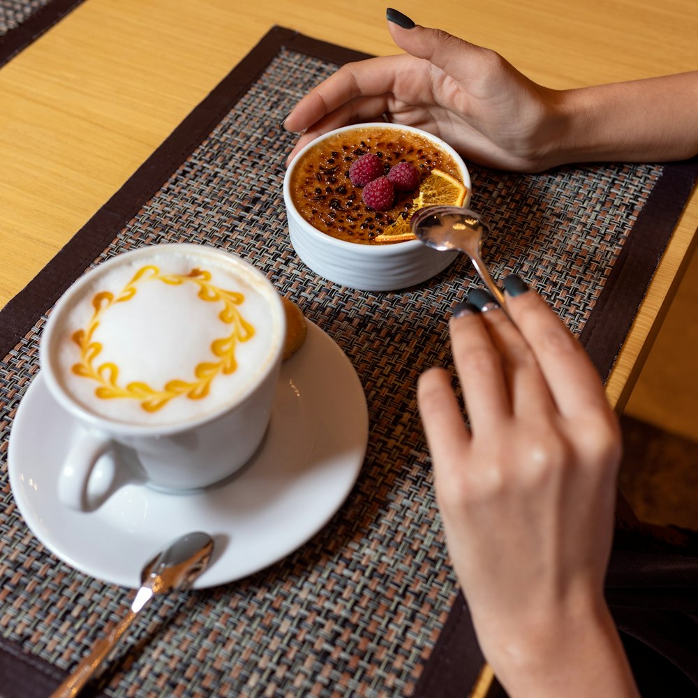 person holding white ceramic cup with saucer and spoon