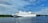 A large white cruise ship with a red and blue stripe moves gracefully across a calm body of water. The ship is detailed with multiple decks and the name 'Cinderella' is visible along the side. In the background, lush green trees line the shoreline under a partly cloudy, blue sky.