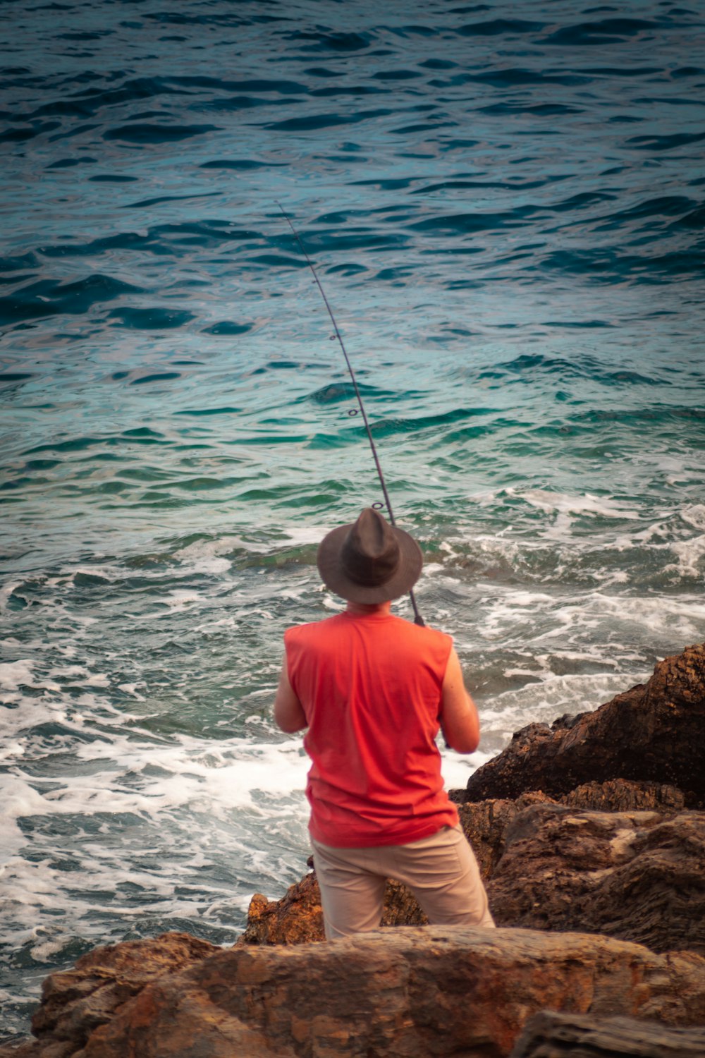 man in orange shirt and white shorts sitting on rock by the sea during daytime