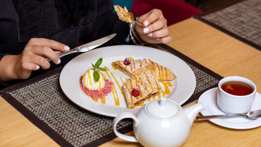 person holding white ceramic teapot pouring white liquid on white ceramic plate