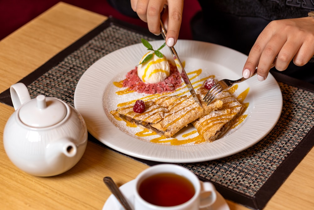 person holding fork and knife slicing food on white ceramic plate